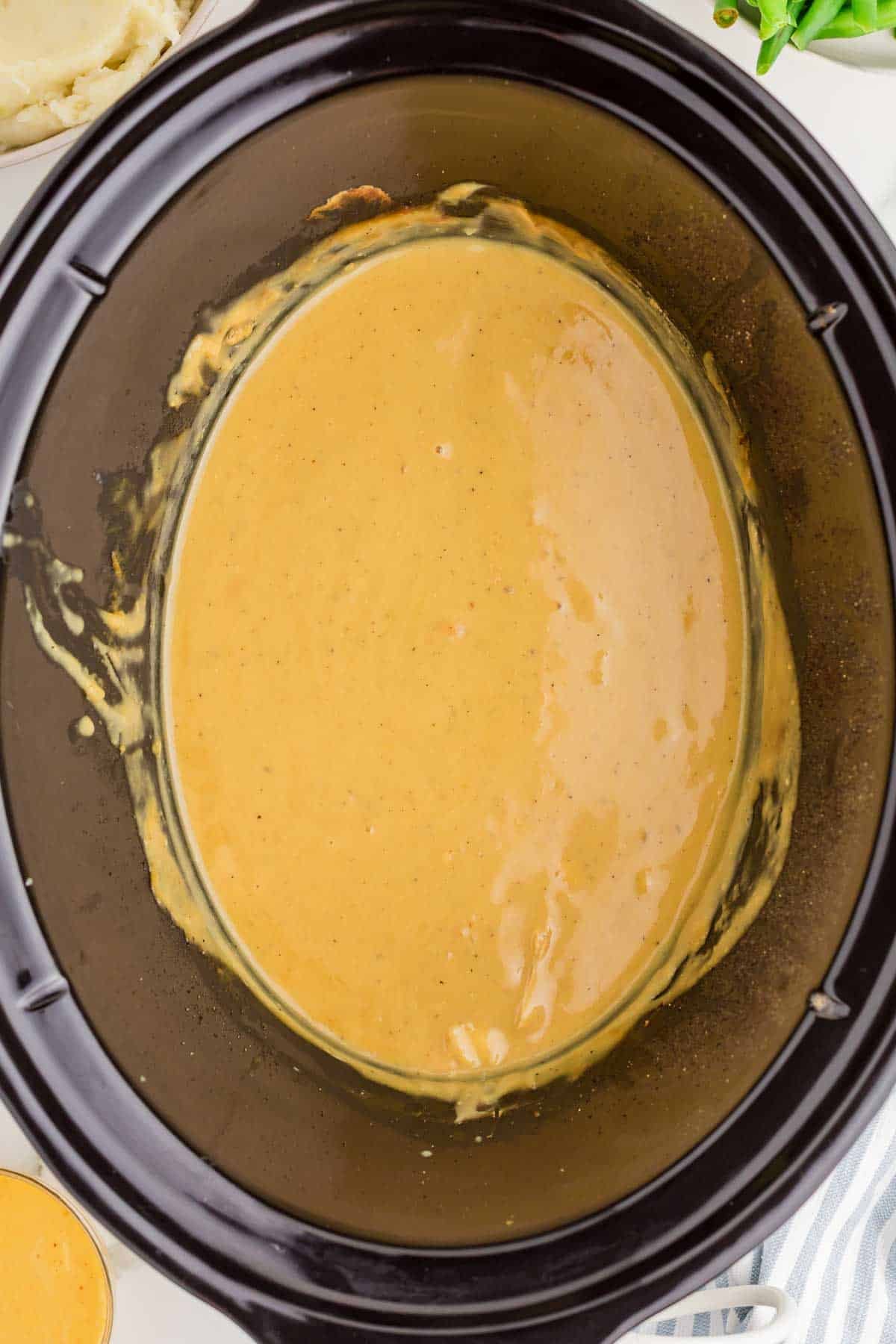 Thickened honey mustard sauce coating the bottom of the slow cooker after the cooked chicken has been removed. The smooth sauce will be mixed with the shredded chicken.