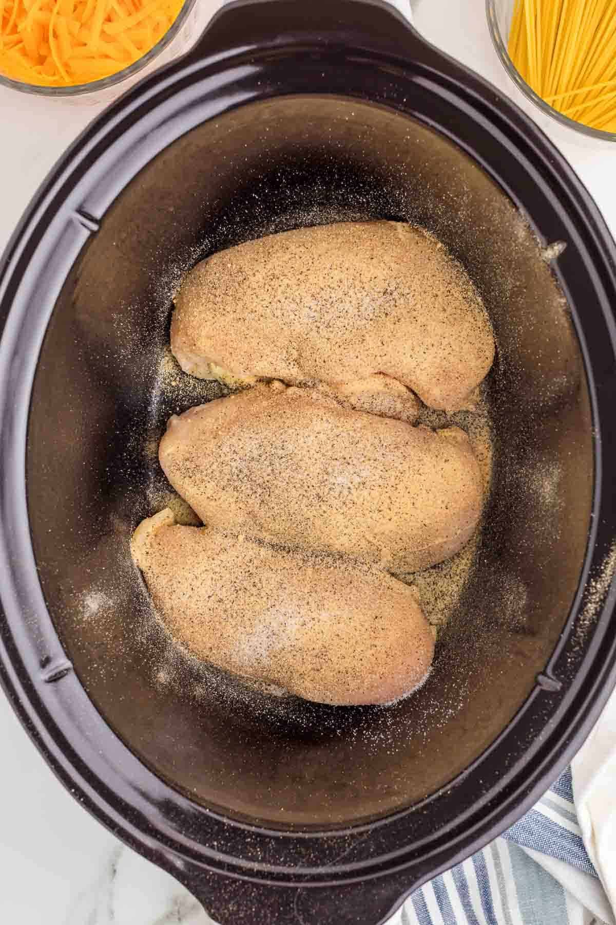 Three chicken breasts in a slow cooker evenly coated with garlic powder onion powder salt and black pepper.