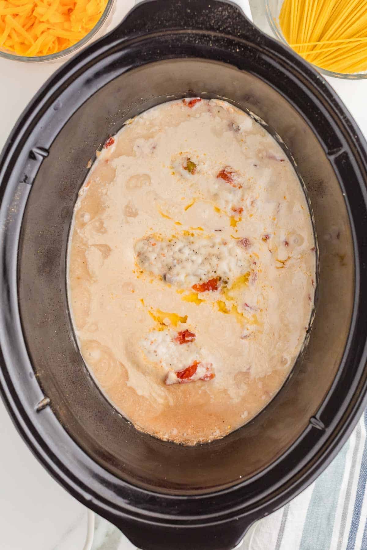Cooked chicken breasts resting in the creamy tomato and mushroom mixture inside the slow cooker before being removed for shredding.