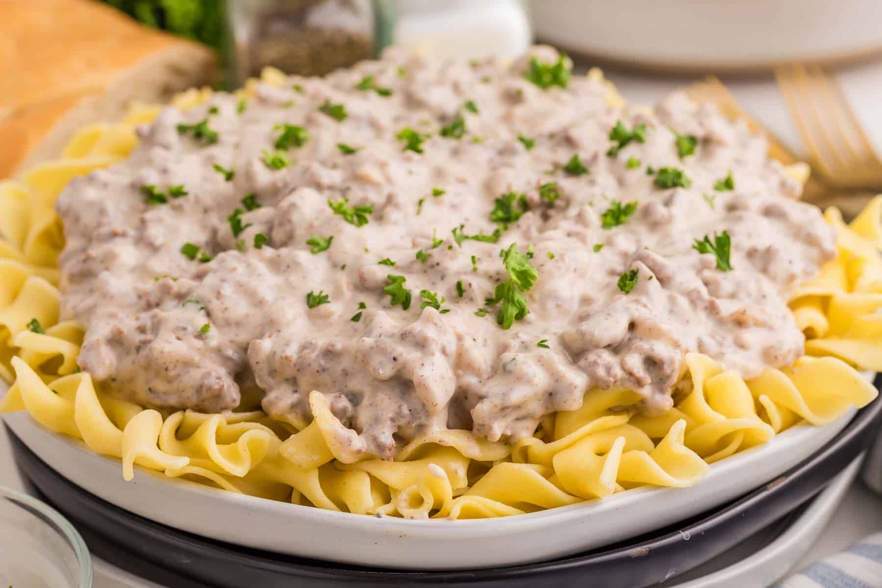 Ground beef stroganoff served over a bed of wide egg noodles with chopped parsley on top. The thick creamy sauce is filled with crumbled ground beef.
