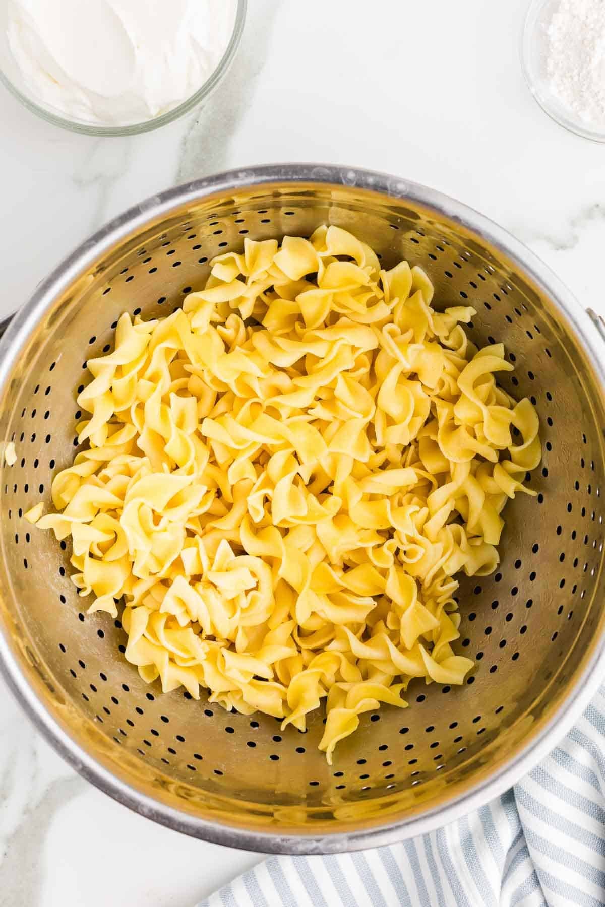 Cooked wide egg noodles draining in a colander. The noodles are ready to be served with the ground beef stroganoff.