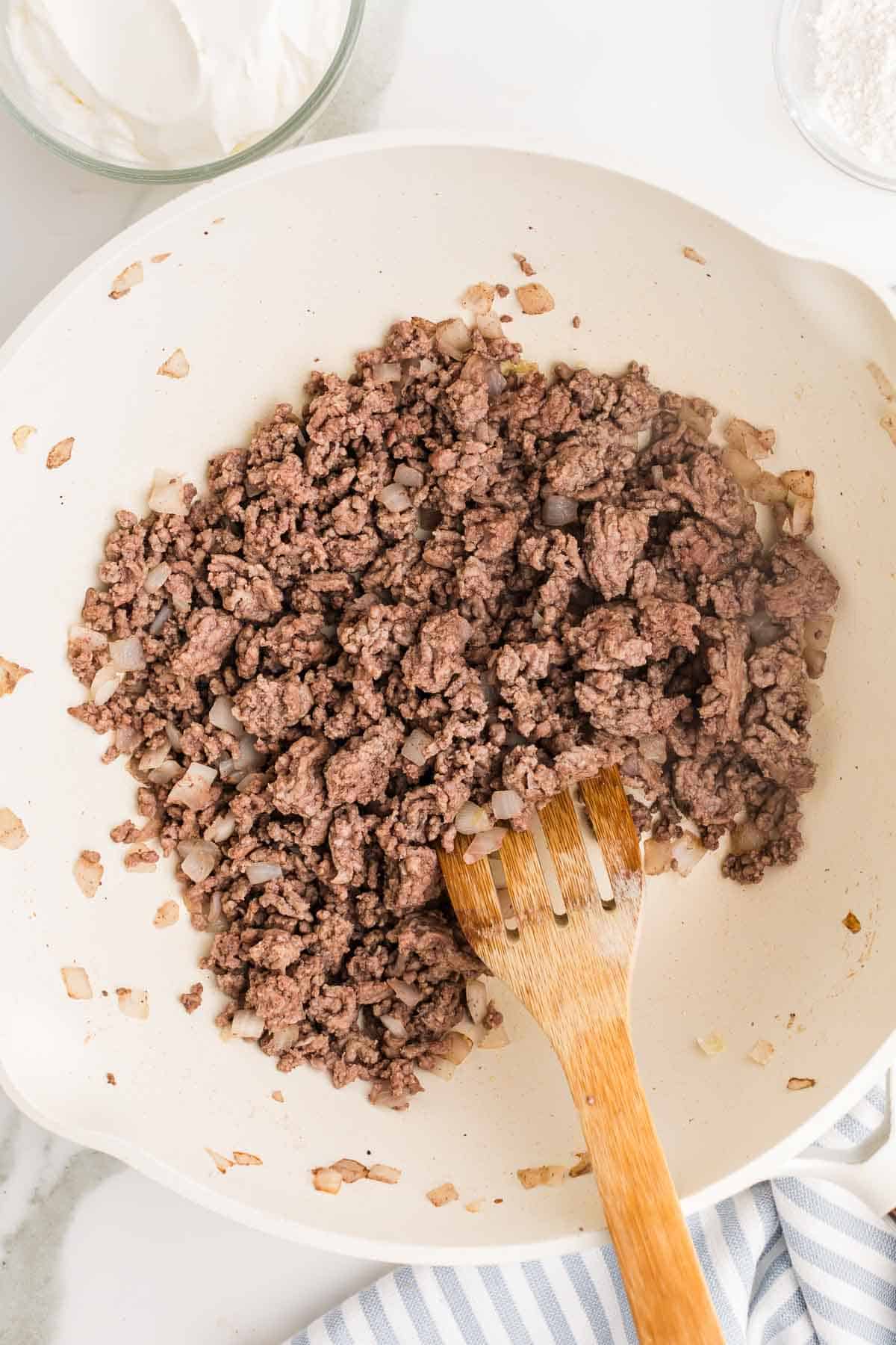 Ground beef and diced onion cooking together in a skillet. The beef has been broken into crumbles and browned.