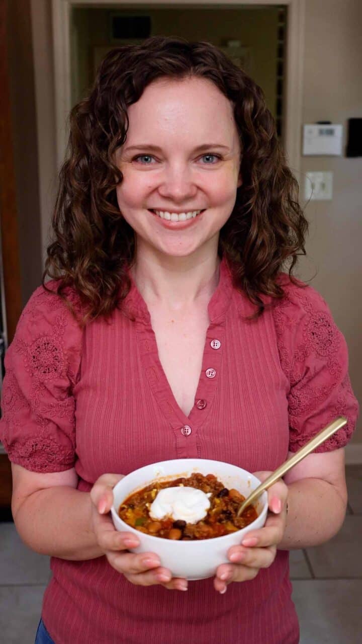 Kelsey Smith holding a small bowl of beef and sausage chili topped with sour cream.