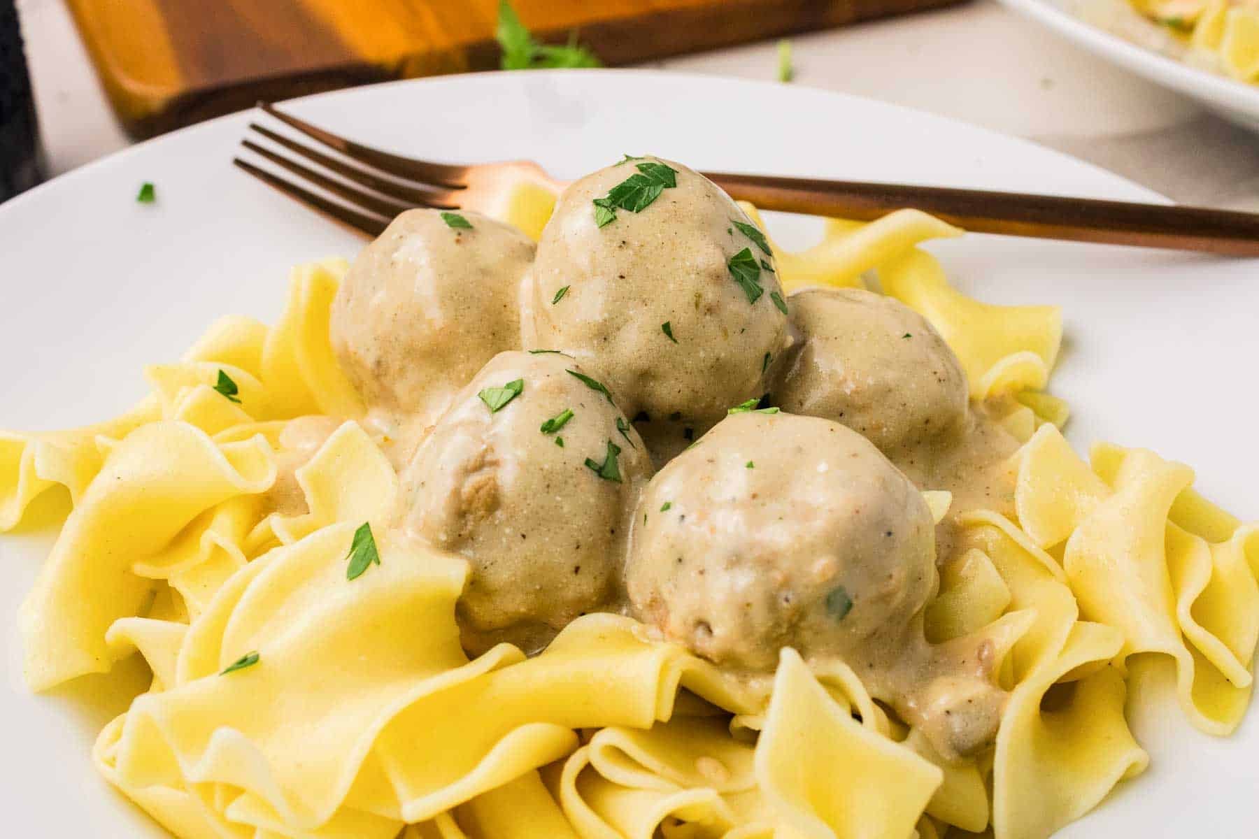 Crockpot Swedish meatballs covered in creamy mushroom sauce and served over cooked egg noodles. Chopped parsley is scattered over the meatballs.