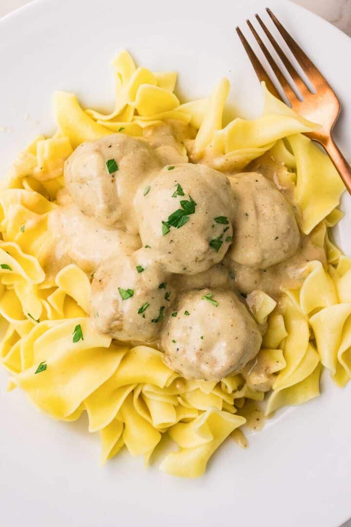Overhead view of Crockpot Swedish meatballs and creamy sauce served over wide egg noodles. Chopped parsley is sprinkled over the finished dish.