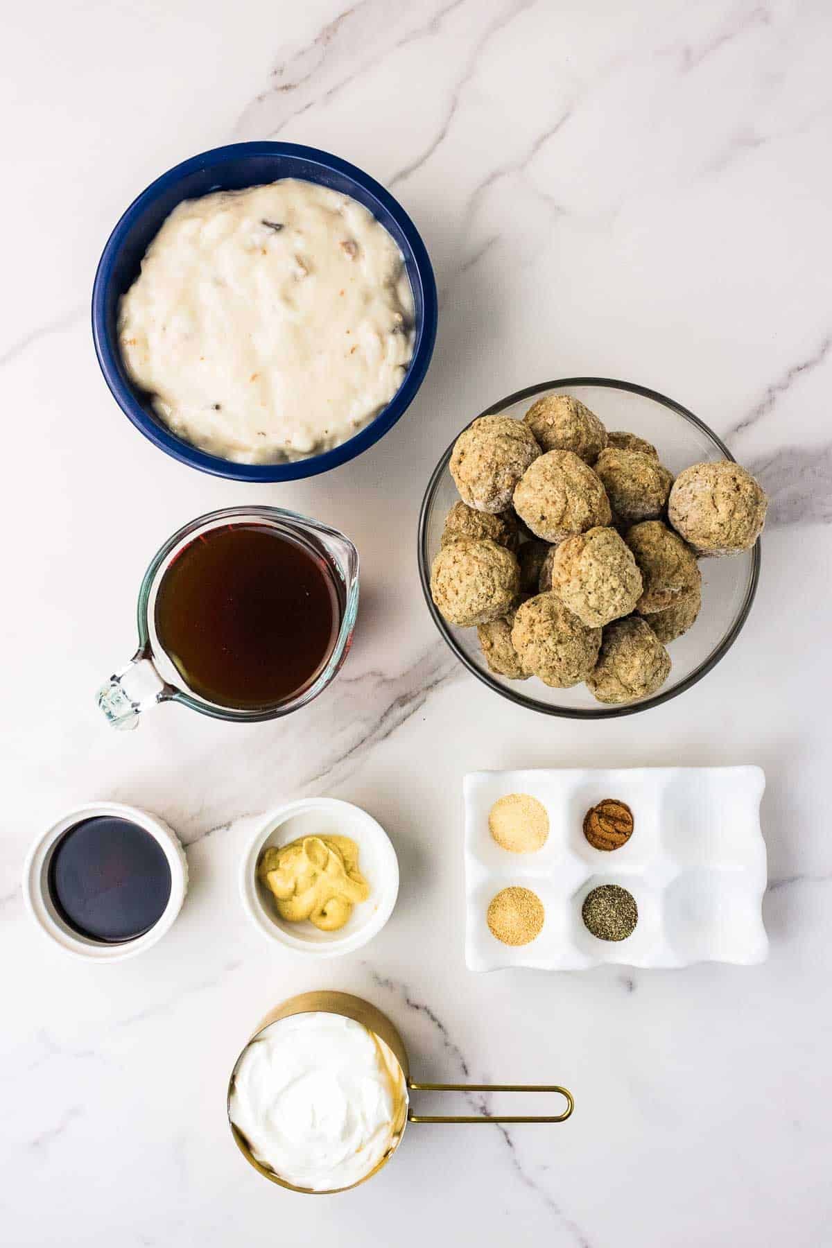Ingredients for Crockpot Swedish meatballs arranged together before cooking. Frozen meatballs sit beside cream of mushroom soup. Beef broth. Worcestershire sauce. Dijon mustard. Garlic powder. Onion powder. Black pepper. Nutmeg. And sour cream.