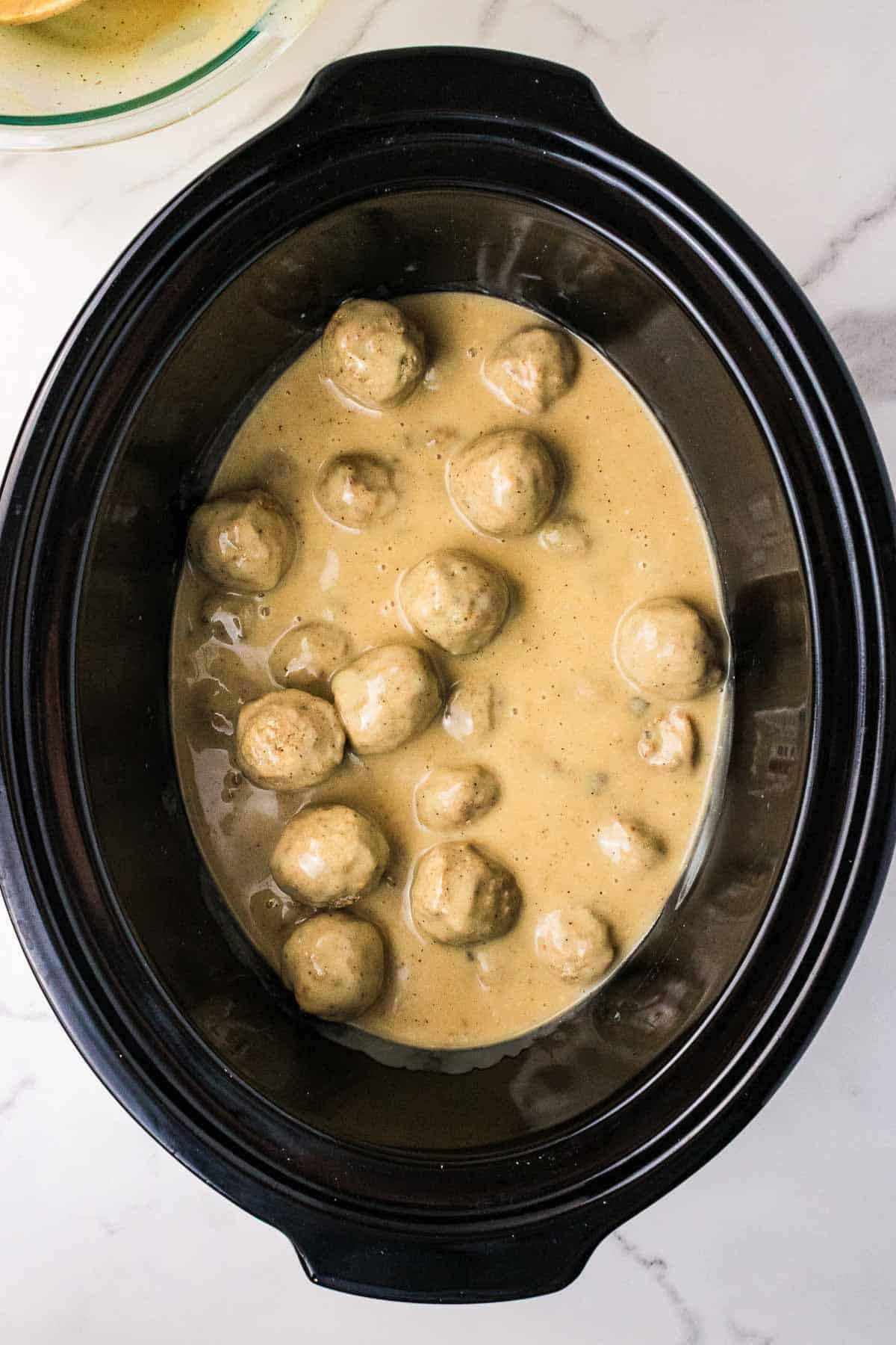 Frozen meatballs cooking in creamy mushroom sauce inside a slow cooker. The meatballs are partially submerged as they heat in the sauce.