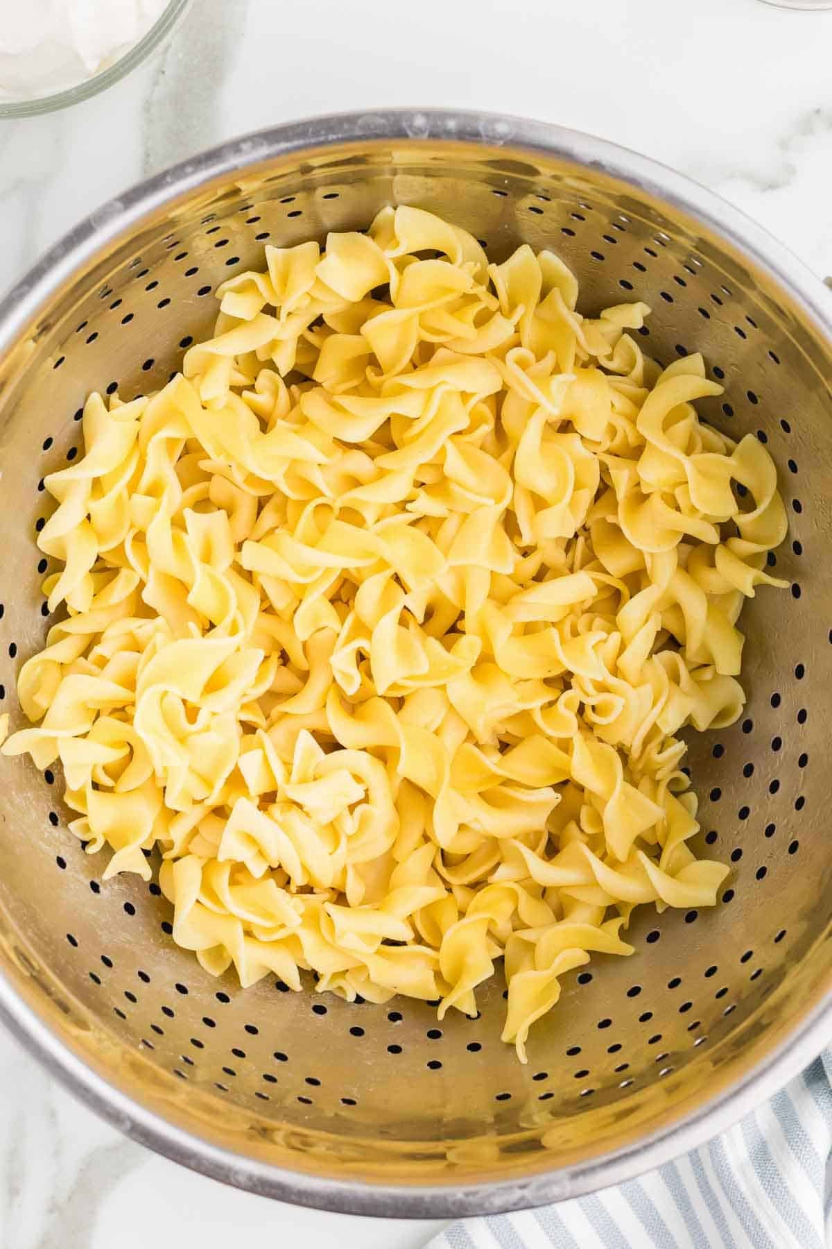 Cooked egg noodles draining in a colander before serving with the Crockpot Swedish meatballs. The noodles are cooked separately while the meatballs finish in the slow cooker.