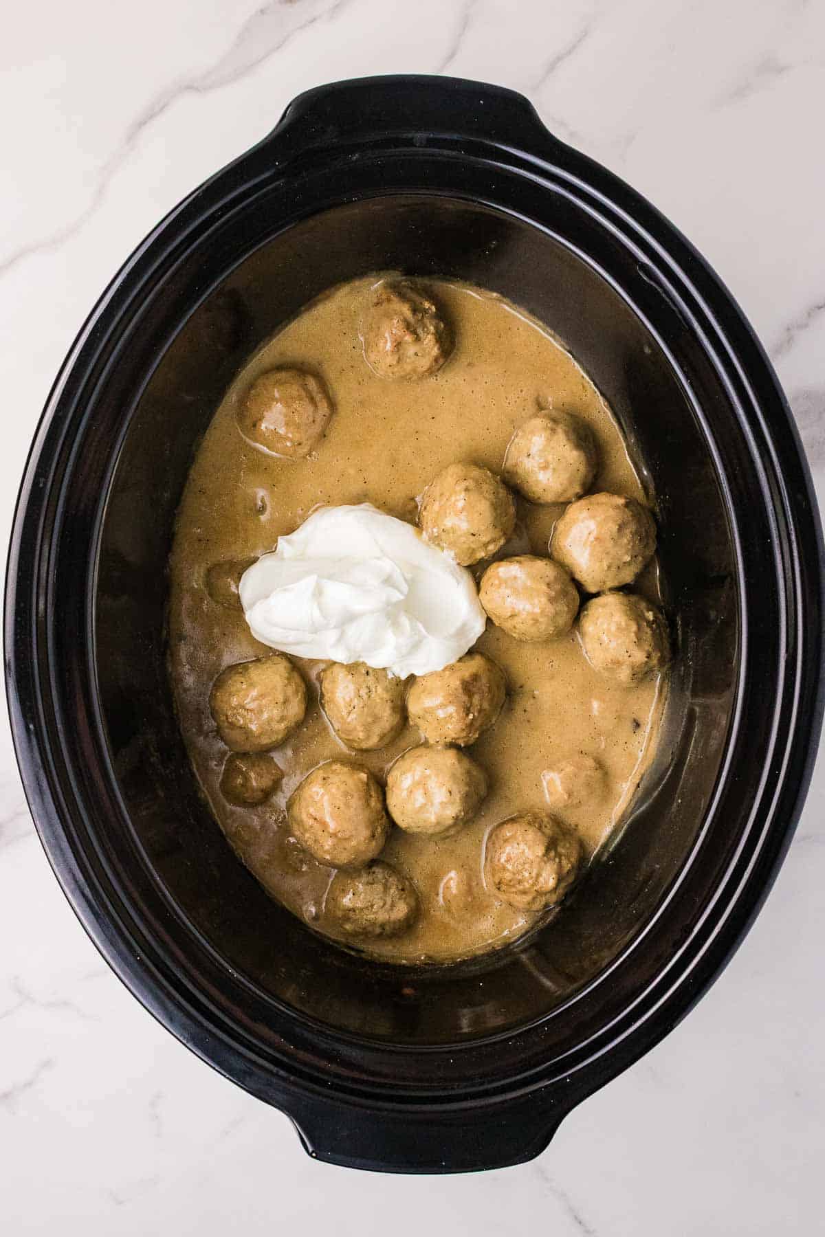Sour cream added to the cooked meatballs and mushroom sauce in the slow cooker. The sour cream will be stirred into the sauce just before serving.