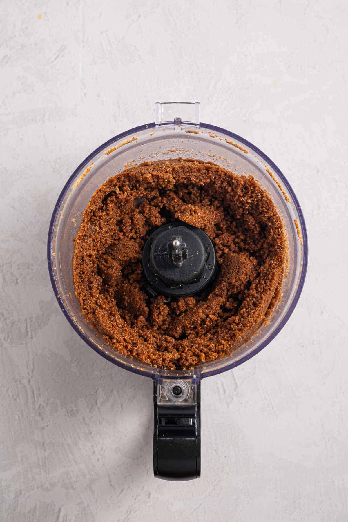 Finely crushed Biscoff cookies mixed with brown sugar and melted butter in a food processor. The moistened crumbs have a wet sand texture and are ready to be pressed into the pie dish.