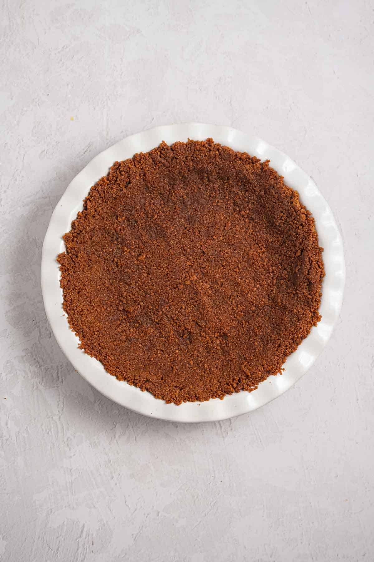 Biscoff cookie crumb mixture pressed firmly across the bottom and up the sides of a pie dish. The even crust is ready to be chilled until firm.