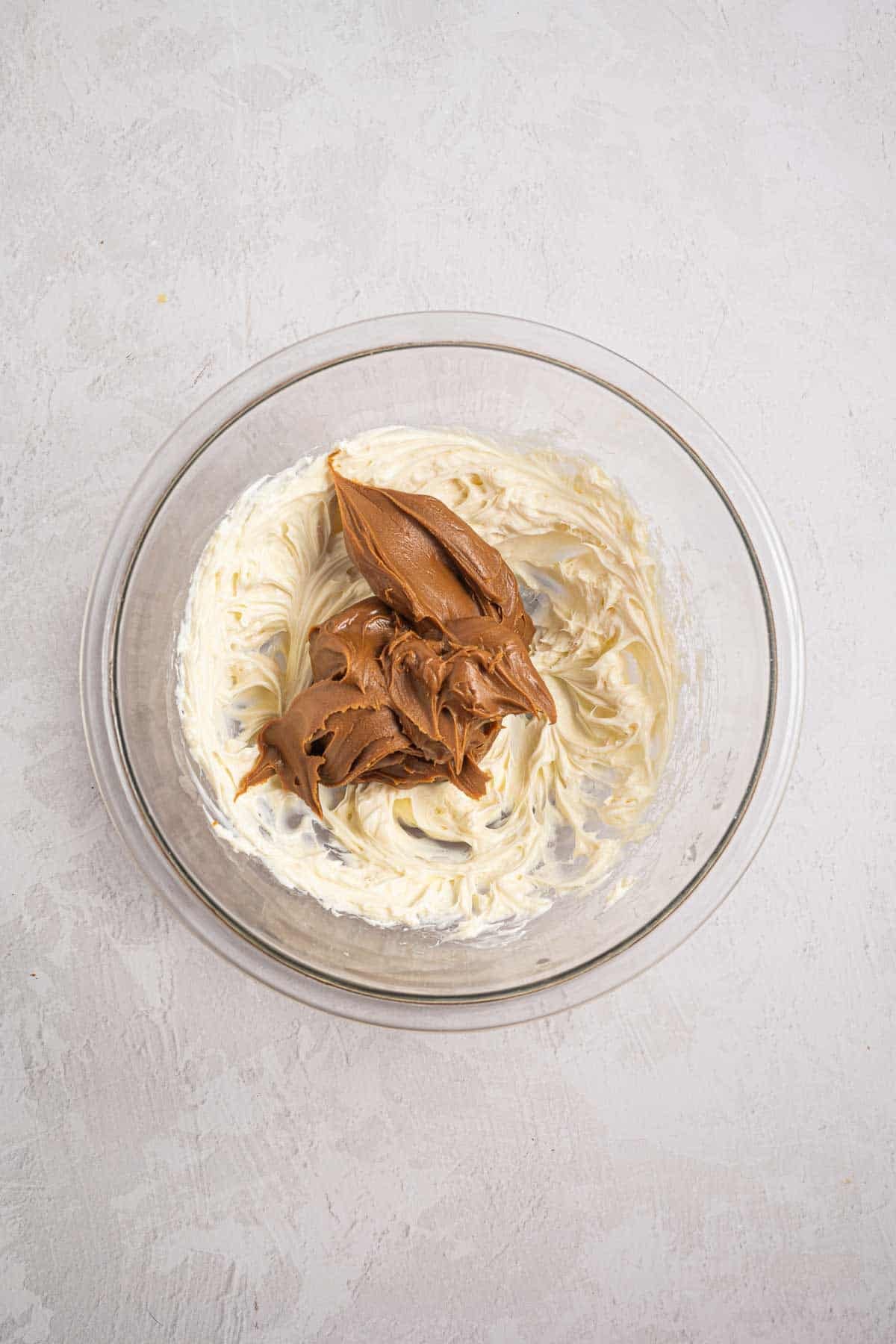 Cookie butter added to a bowl of beaten cream cheese mixture. The two mixtures are ready to be beaten together for the pie filling.
