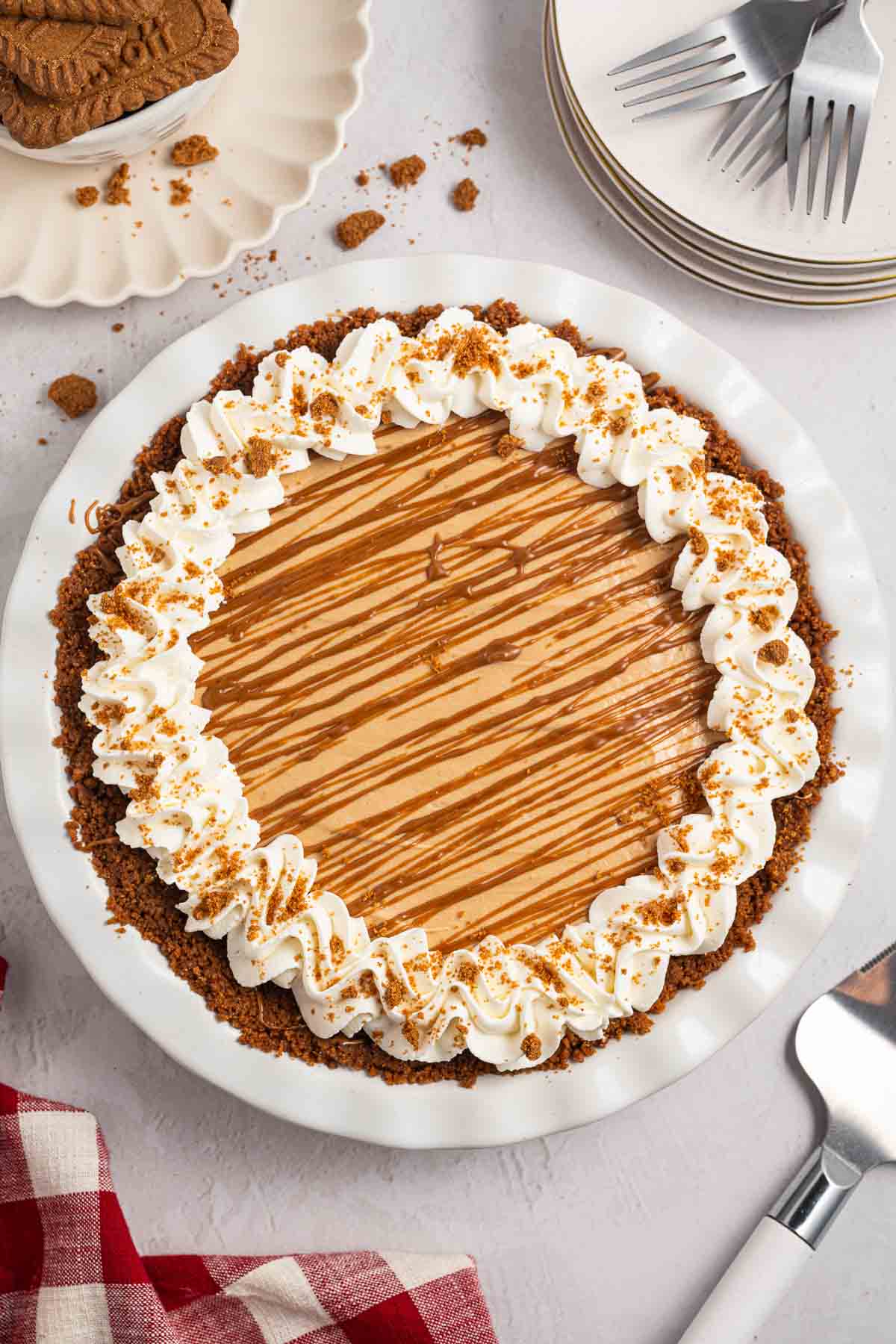 Whole no bake Biscoff cookie butter pie topped with a ring of whipped cream and crushed Biscoff cookies. Melted cookie butter is drizzled across the smooth filling.