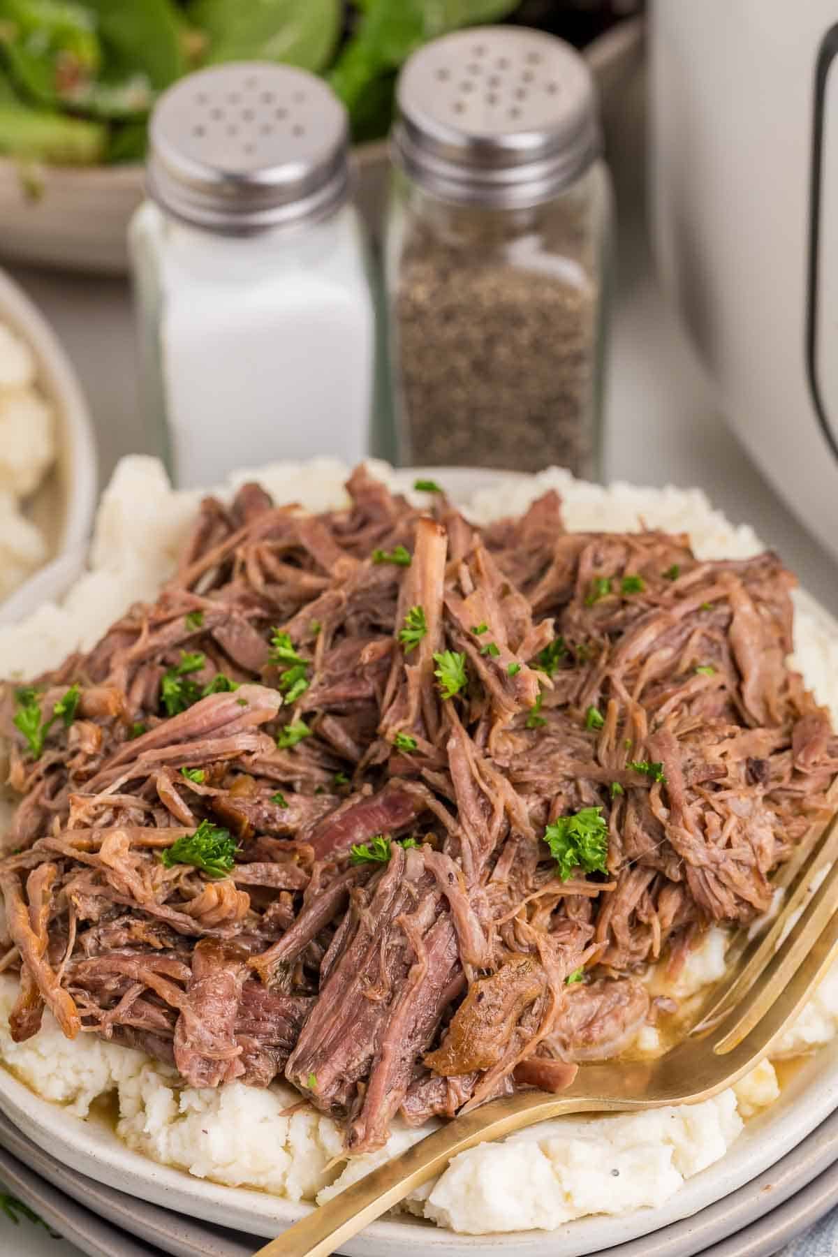 Shredded Mississippi pot roast is piled over creamy mashed potatoes and garnished with chopped parsley.