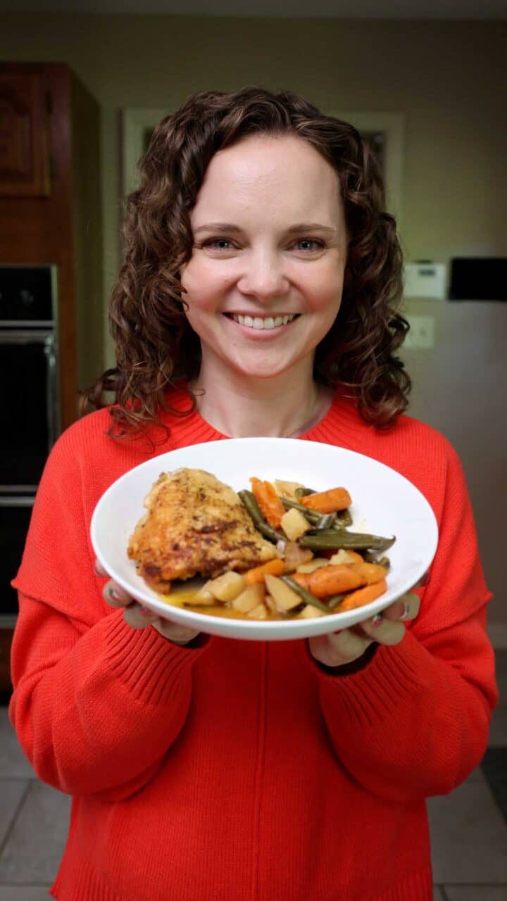 Kelsey Smith holding a shallow bowl of chicken thighs and veggies.