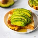 A slice of toast topped with thick slices of avocado, sea salt, course black pepper, and a drizzle of honey