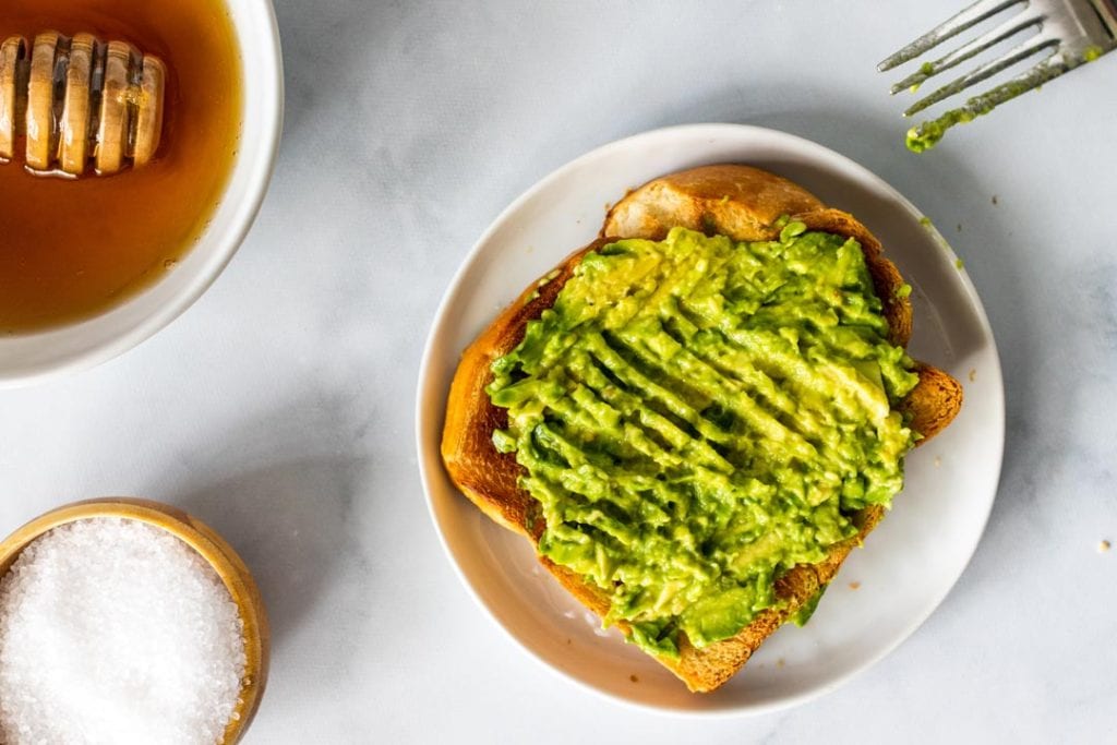 A slice of toast with mashed avocado on top and a fork off to the side