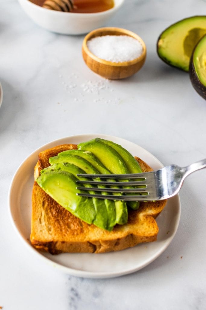 A fork sitting on top of thick slices of avocado on top of a piece of toast