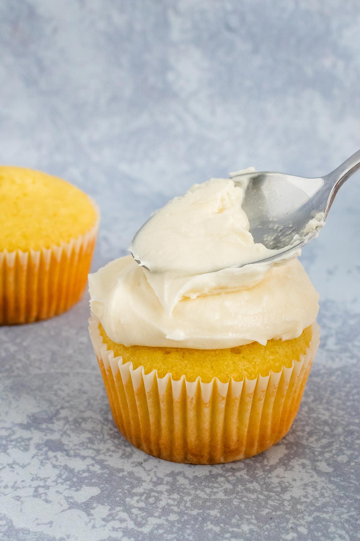 Frosting a cupcake with buttercream using a spoon.