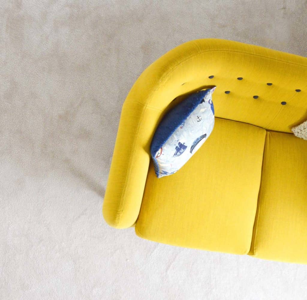 Top-view of a yellow couch with a blue pillow.