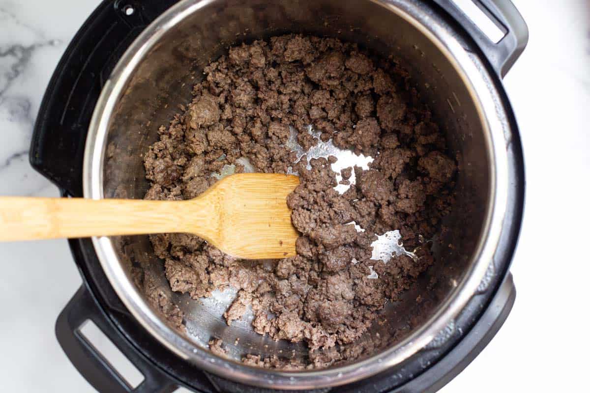 Browned ground beef in the Instant Pot with a wooden spoon.