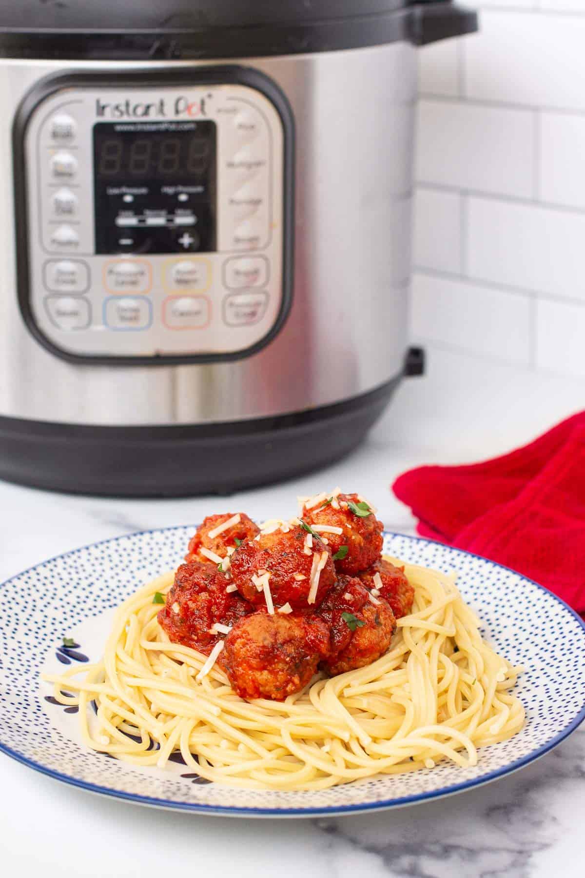 A pile of cooked spaghetti on a small plate topped with meatballs covered in marinara with an Instant Pot in the background.