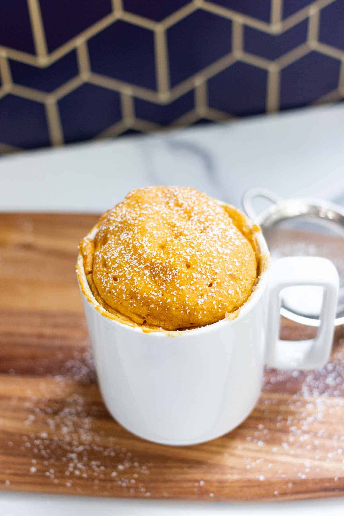 Pumpkin spice mug cake cooled and dusted with powdered sugar.