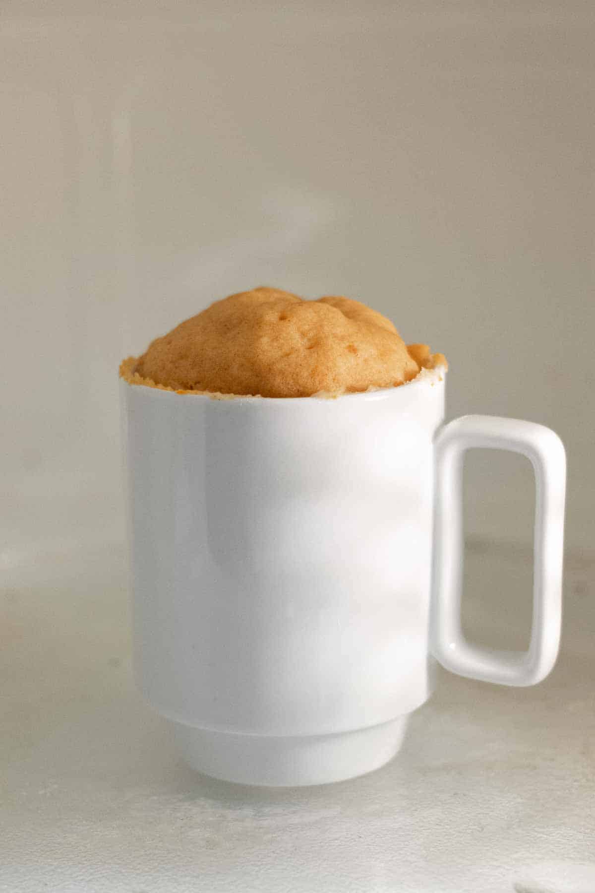 Cooked cake risen over edge of mug just after microwaving.