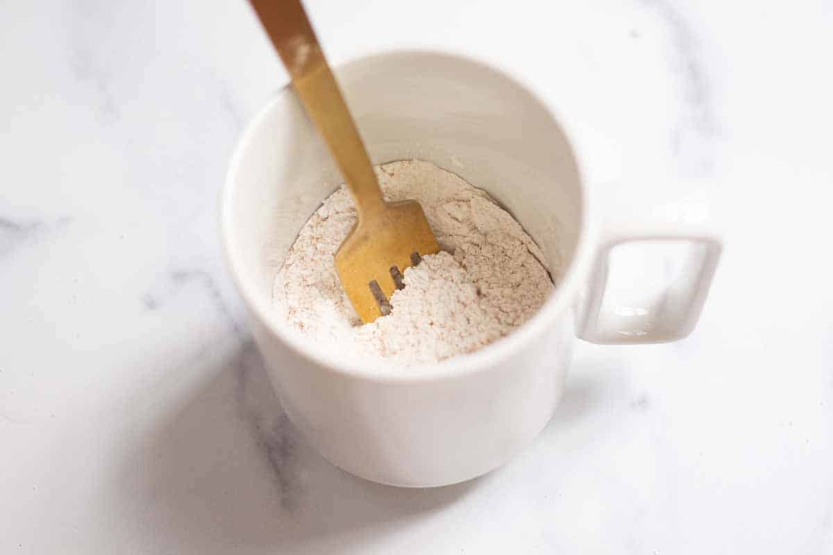 Pumpkin spice mug cake dry ingredients mixed in a 12 oz mug with a fork.