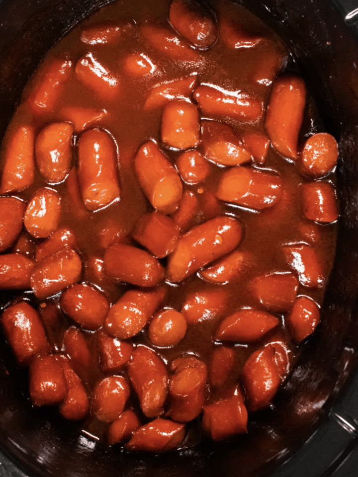 Hot dogs cut in small bite size pieces covered in BBQ sauce in a slow cooker.