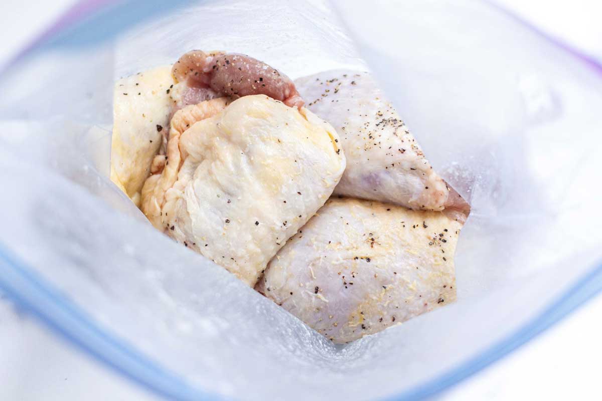 Raw bone in skin on chicken thighs covered in seasoning in a gallon size bag.