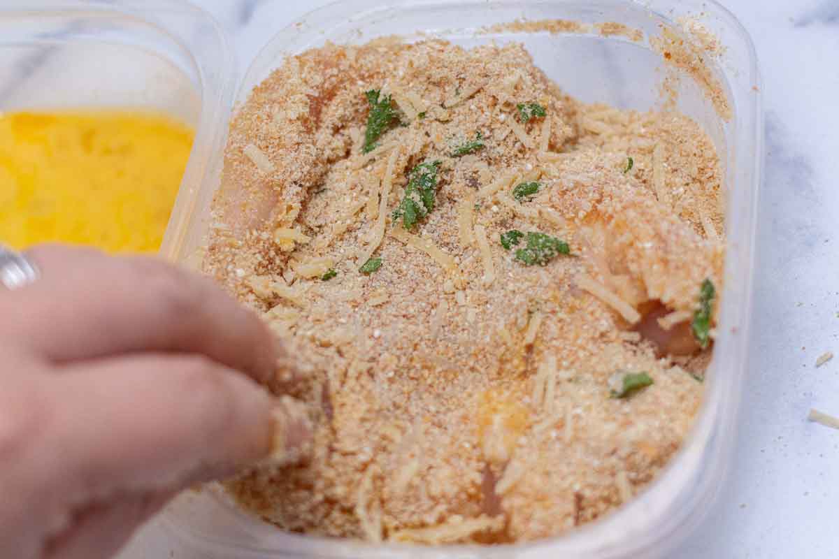 Pressing raw chicken into breadcrumbs to evenly coat.