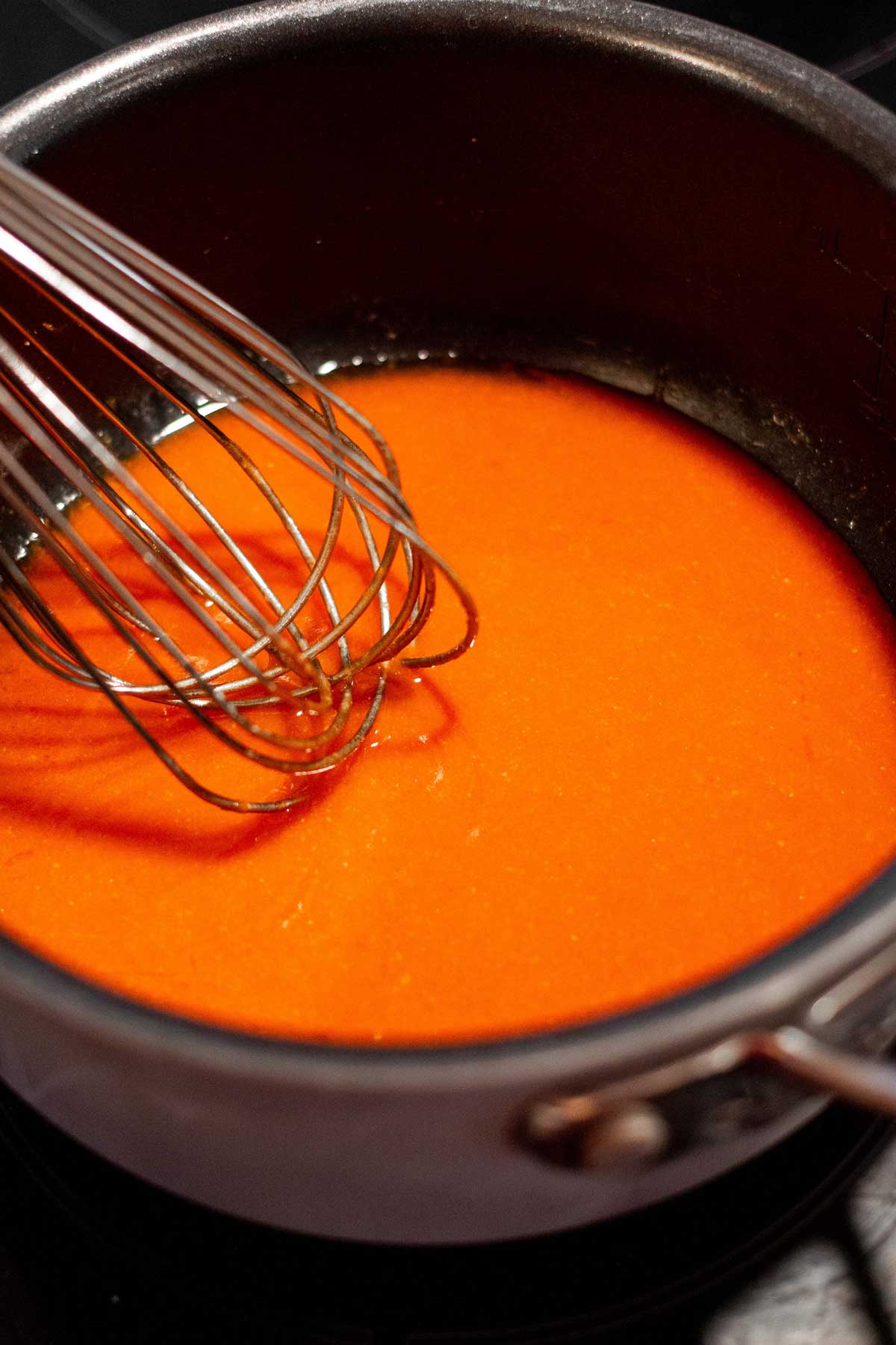 Buffalo sauce in a small sauce pan with a whisk mixing the sauce.