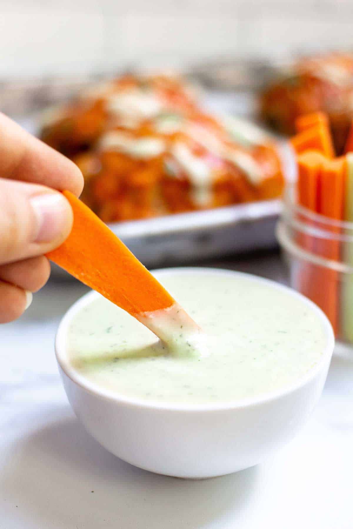 Carrot stick being dipped into small bowl of avocado lime ranch dressing.