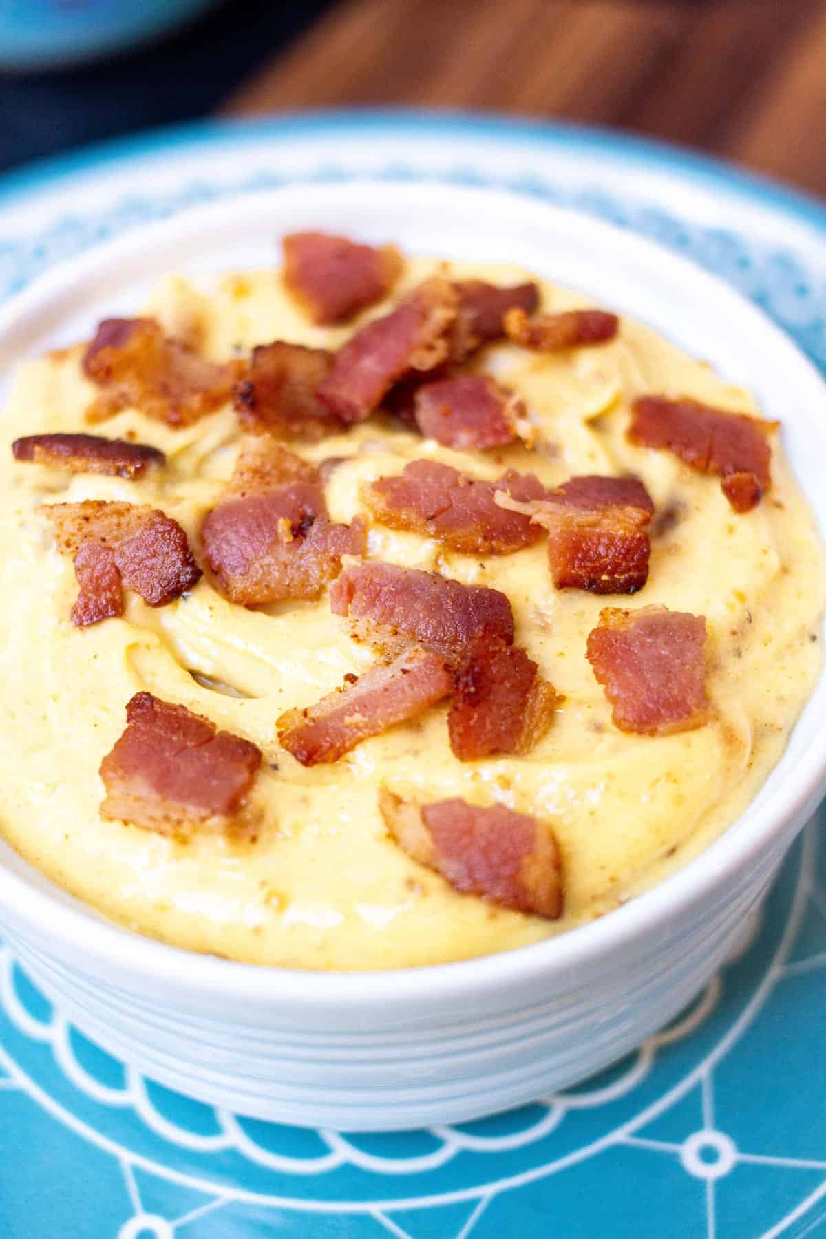 Close up of bacon aioli in a small ramekin topped with cooked bacon bits.