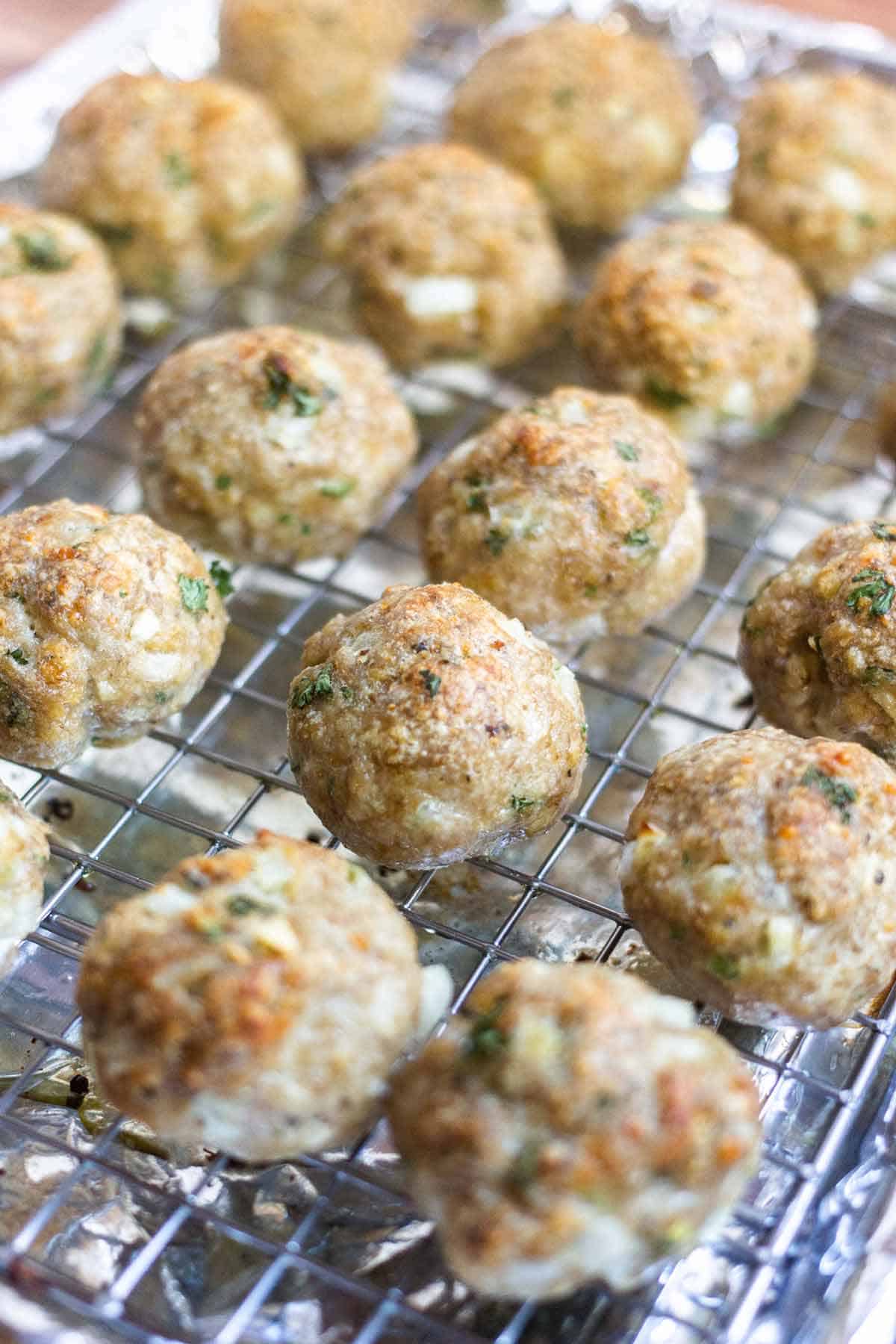 Baked turkey meatballs on a wire rack on a baking tray that is covered in foil.