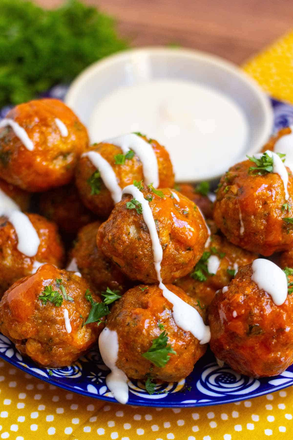 Buffalo turkey meatballs garnished with fresh parsley on a small plate with a small dish of ranch. The meatballs are drizzled in ranch.