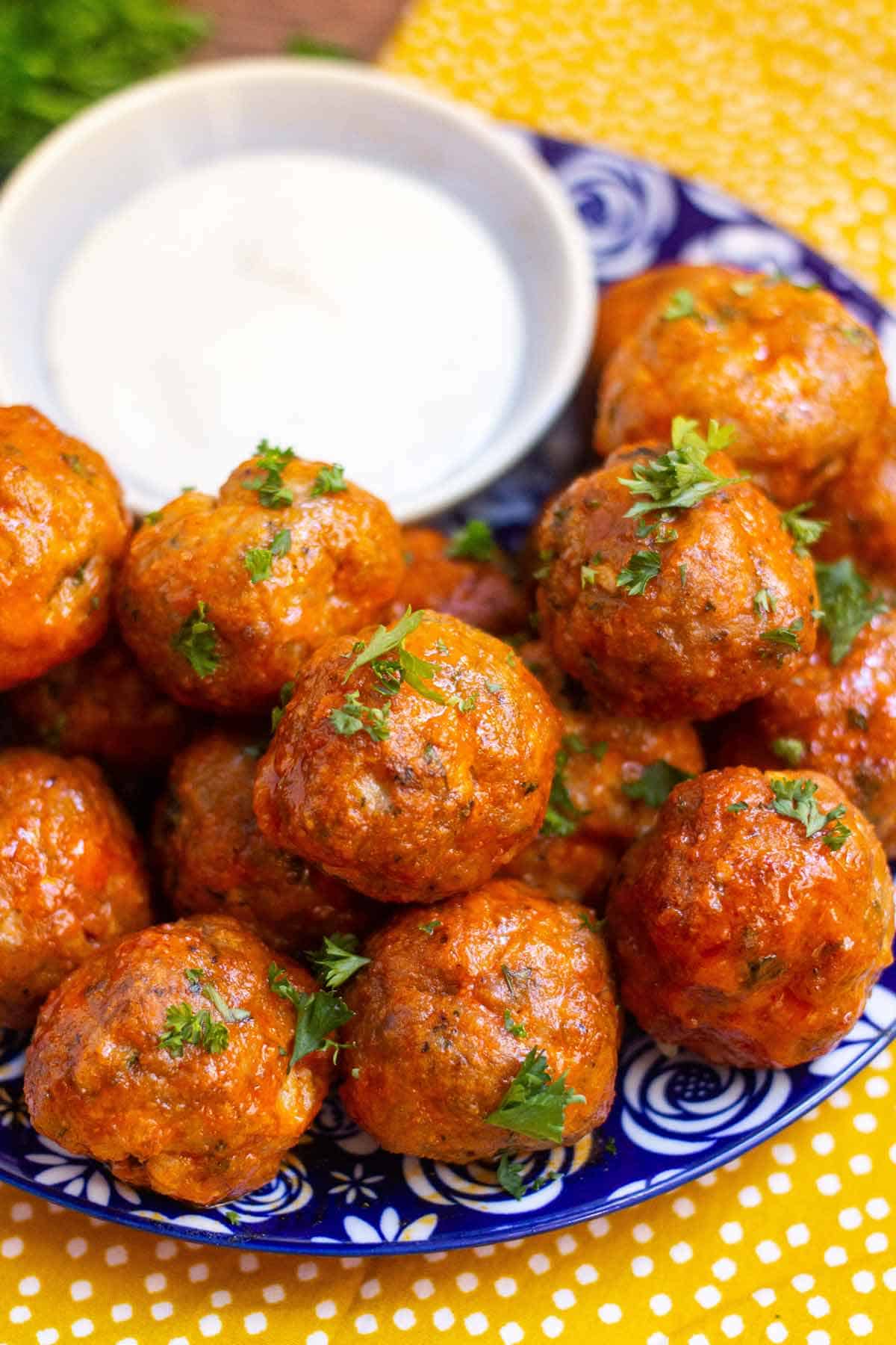 Buffalo turkey meatballs garnished with fresh parsley on a small plate with a small dish of ranch.