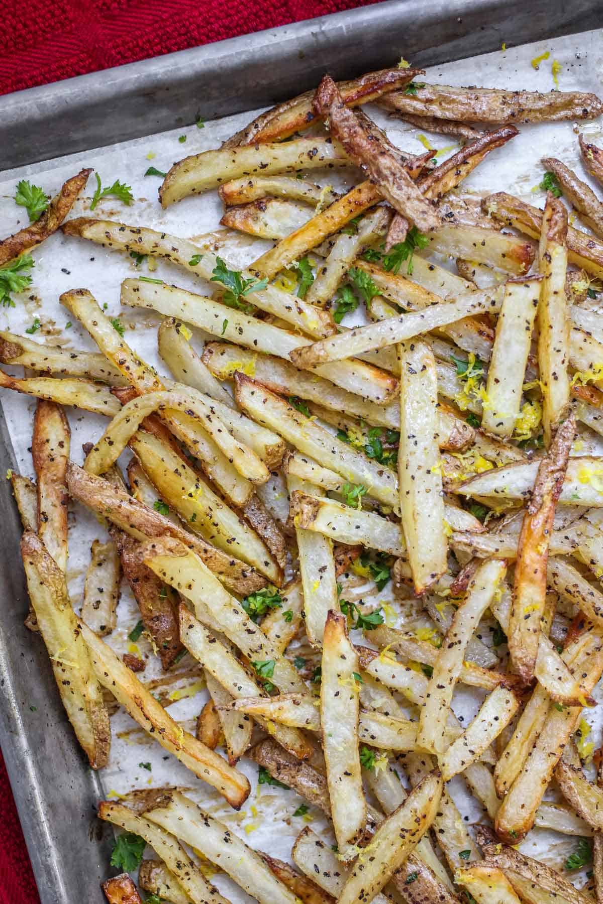 Lemon pepper fries topped with fresh parsley on a baking sheet lined with parchment paper.