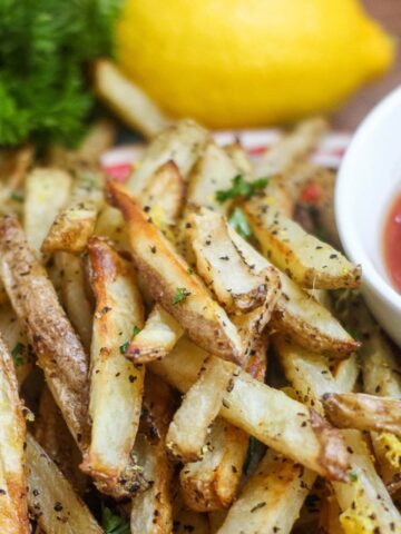 Close up of lemon pepper fries topped with fresh parsley on a plate with a side of ketchup.