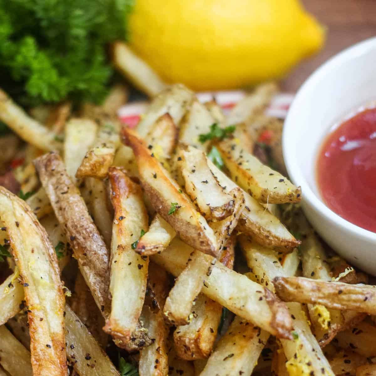 Close up of lemon pepper fries topped with fresh parsley on a plate with a side of ketchup.