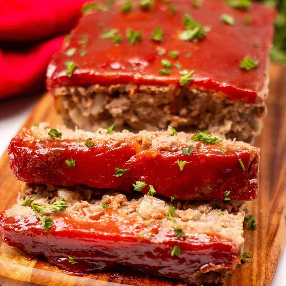 Meatloaf on a cutting board garnished with fresh parsley. Two one-inch slices are cut off the loaf.