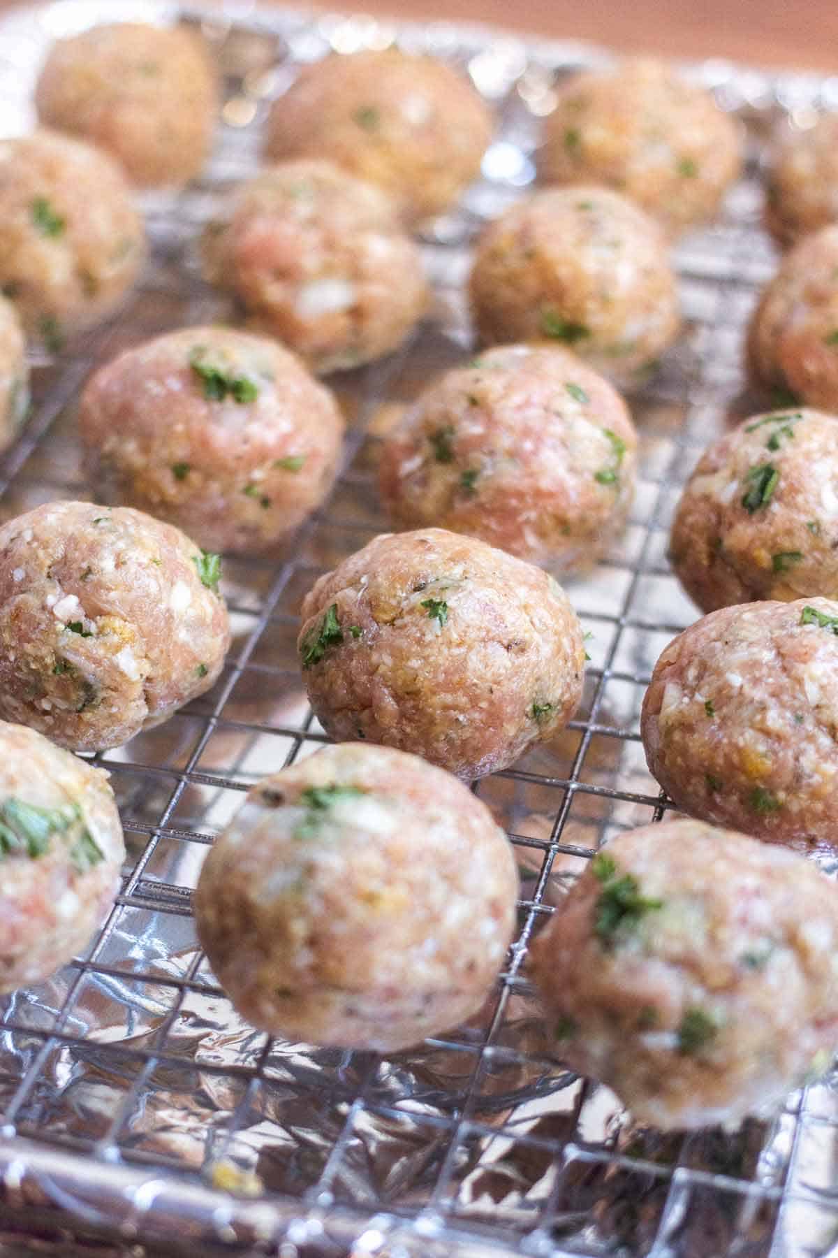 Raw turkey meatballs on a wire rack on a baking tray that is covered in foil.