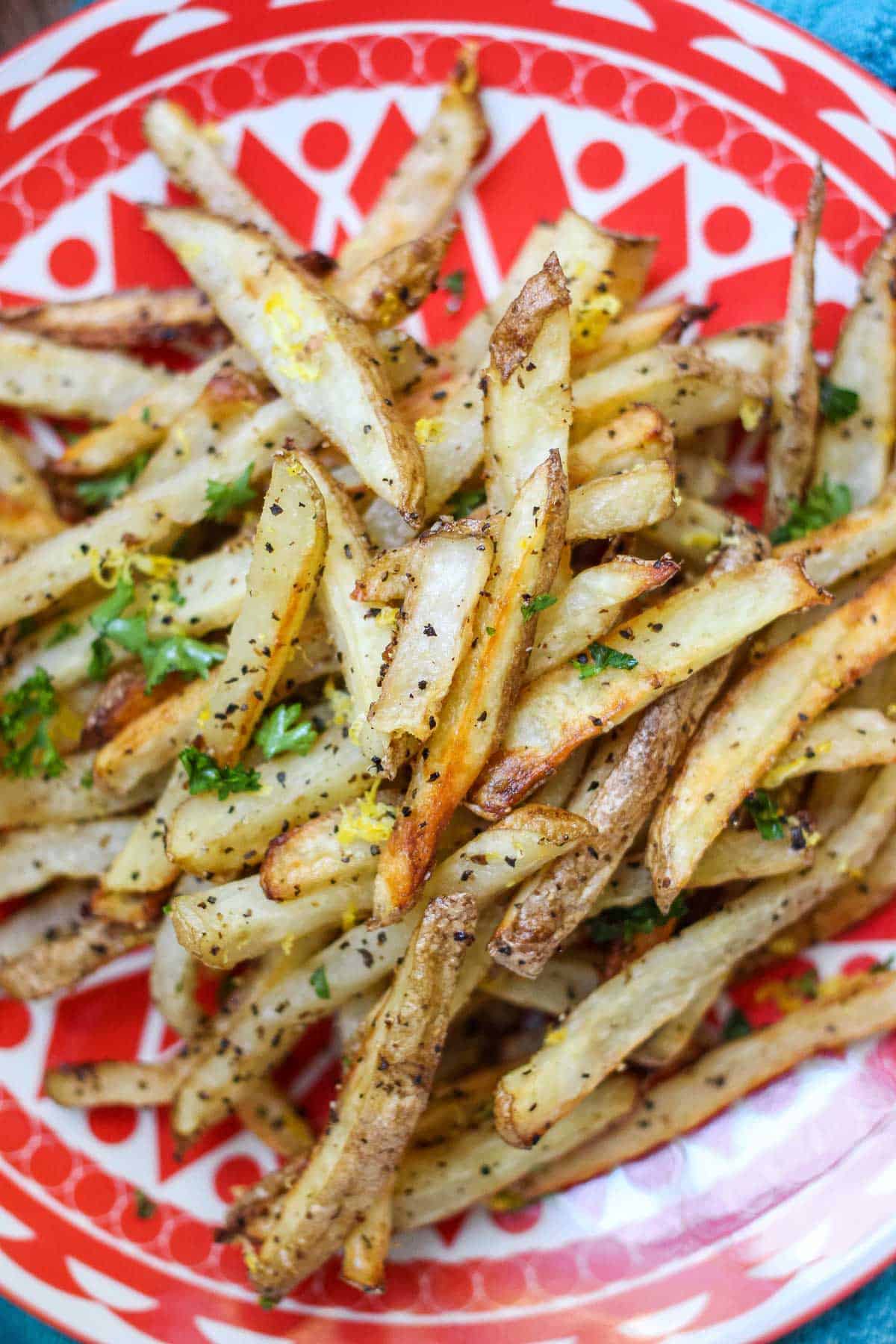 Close up of lemon pepper fries topped with fresh parsley on a plate.
