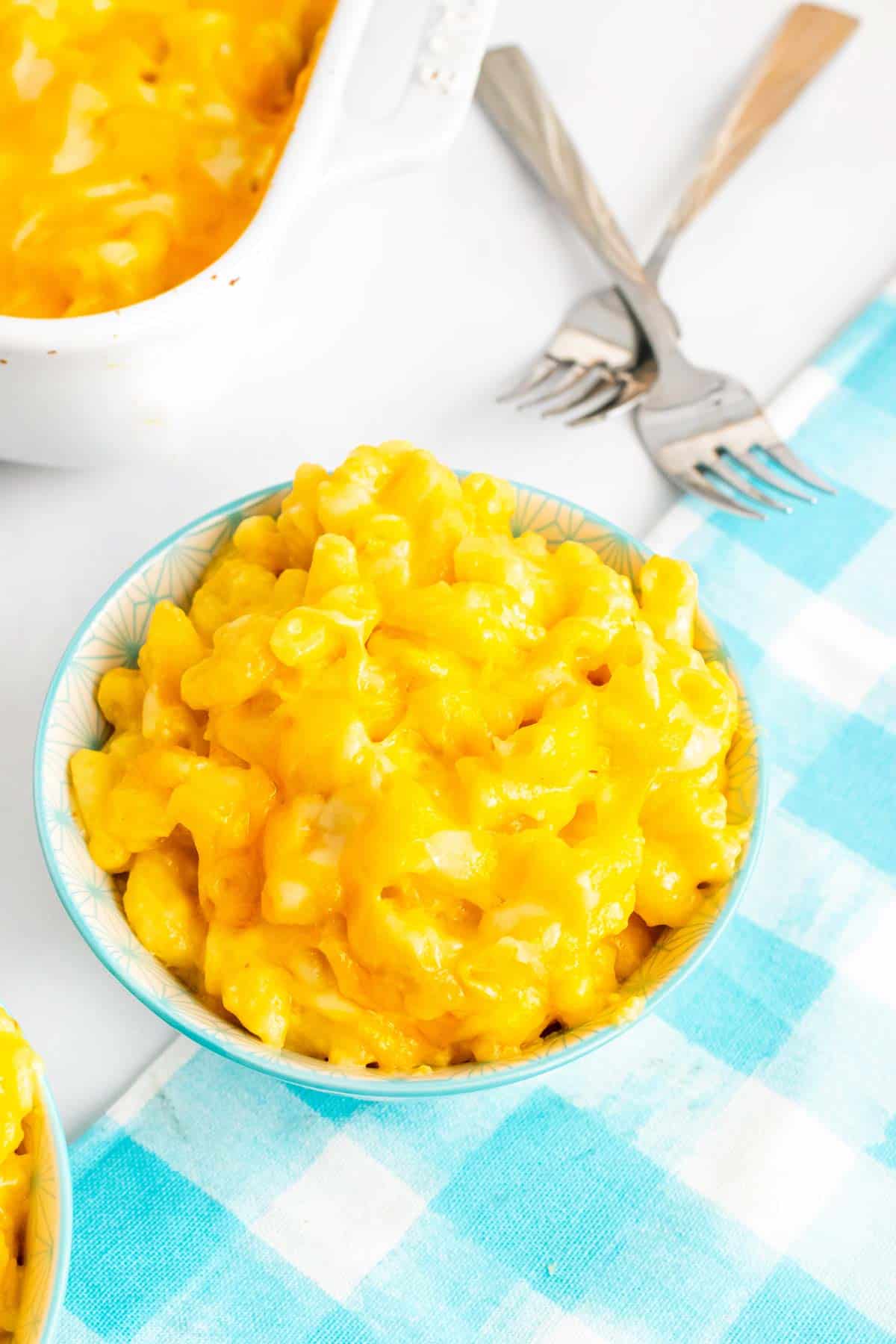 Extra creamy, cheesy macaroni and cheese in a small bowl next to a baking dish of mac and cheese.