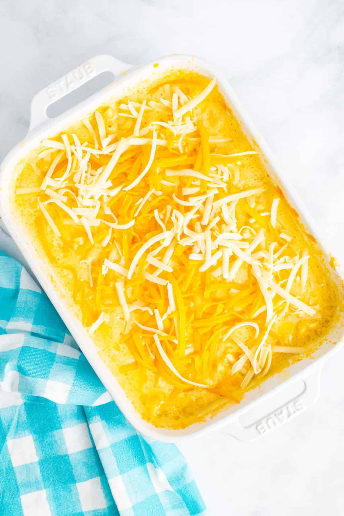 The remaining shredded cheddar and mozzarella cheese are sprinkled on top of the partially baked macaroni and cheese dish.