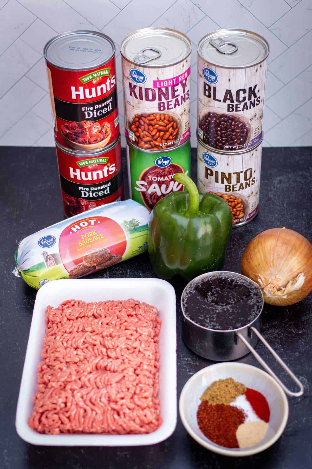 Classic beef and sausage chili ingredients: ground beef, hot pork sausage, beef stock, onion, green bell pepper, black beans, pinto beans, light red kidney beans, tomato sauce, fire roasted diced tomatoes, and seasoning.