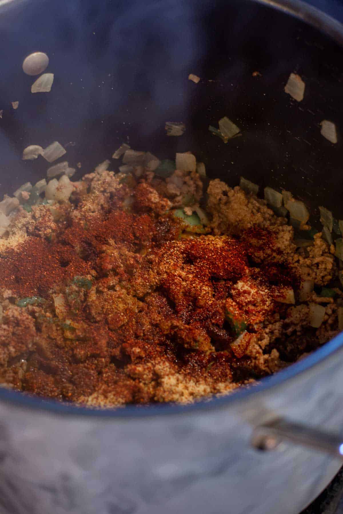 Chili seasoning sprinkled on top of browed ground beef and sausage in a stock pot.