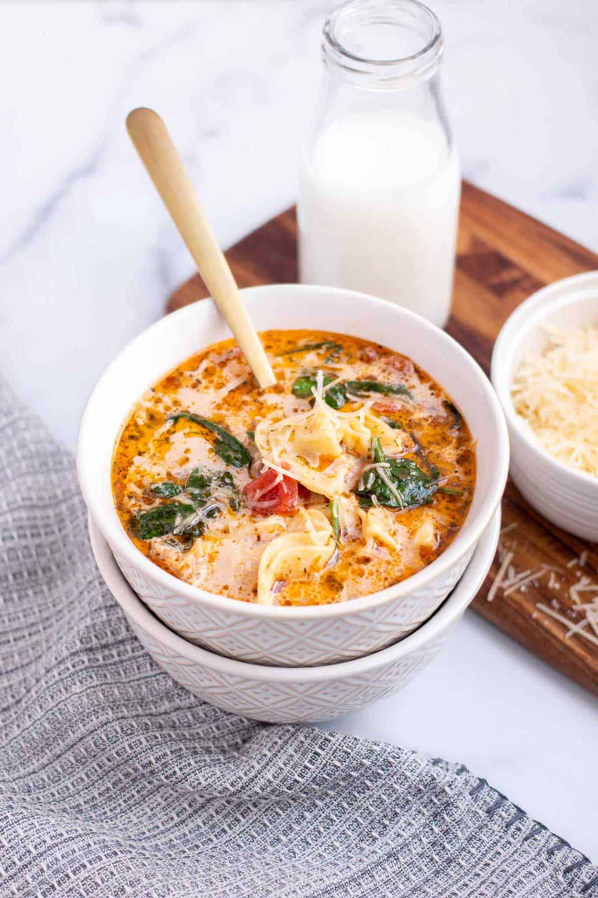 Instant Pot Tortellini Soup with tortellini, Italian sausage, and wilted baby spinach in a bowl garnished with shredded parmesan.