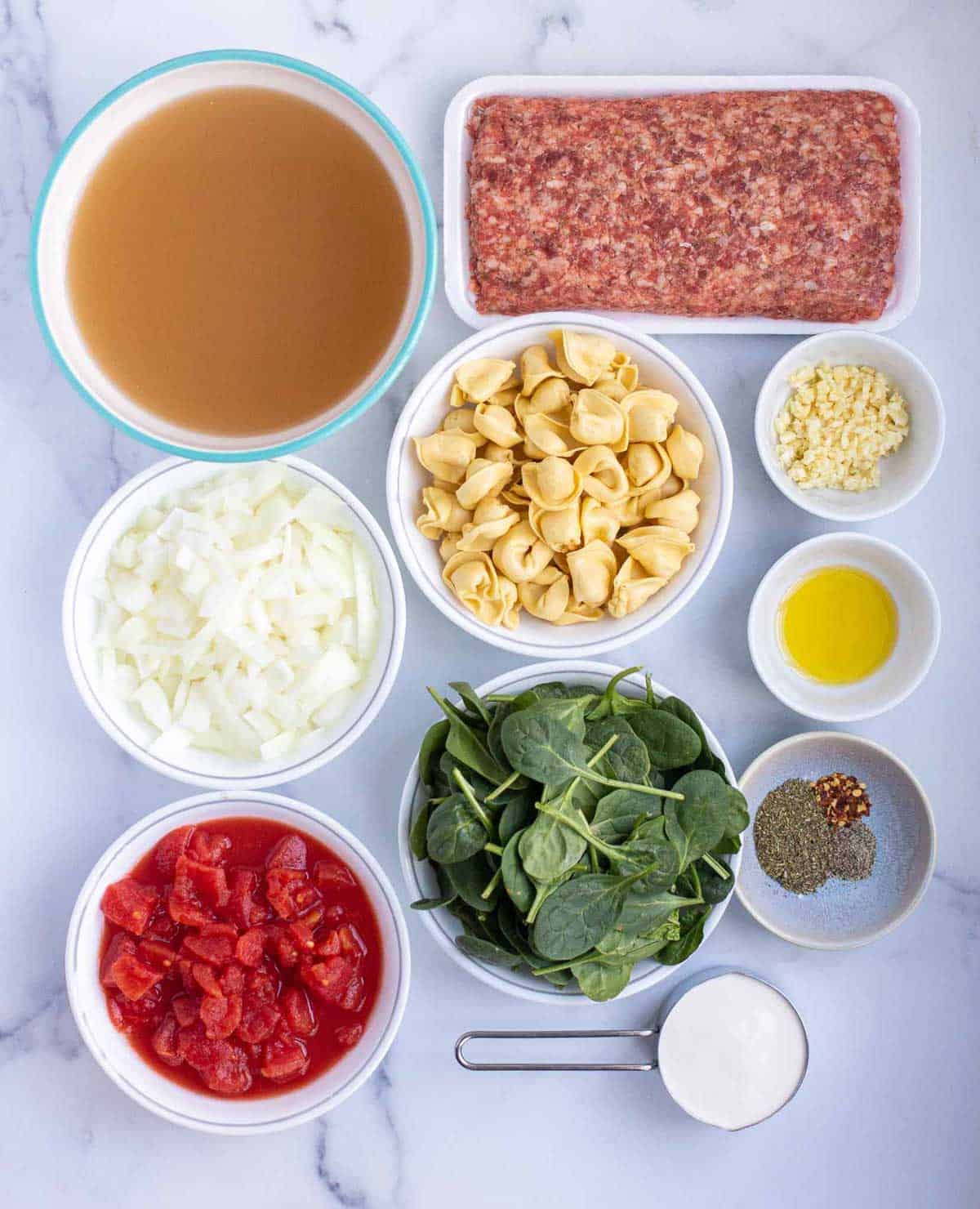 Instant Pot Tortellini Soup ingredients: chicken broth, Italian sausage, cheese tortellini, diced yellow onion, minced garlic, olive oil, fresh baby spinach, diced tomatoes, ground black pepper, crushed red pepper, Italian seasoning, and heavy whipping cream.